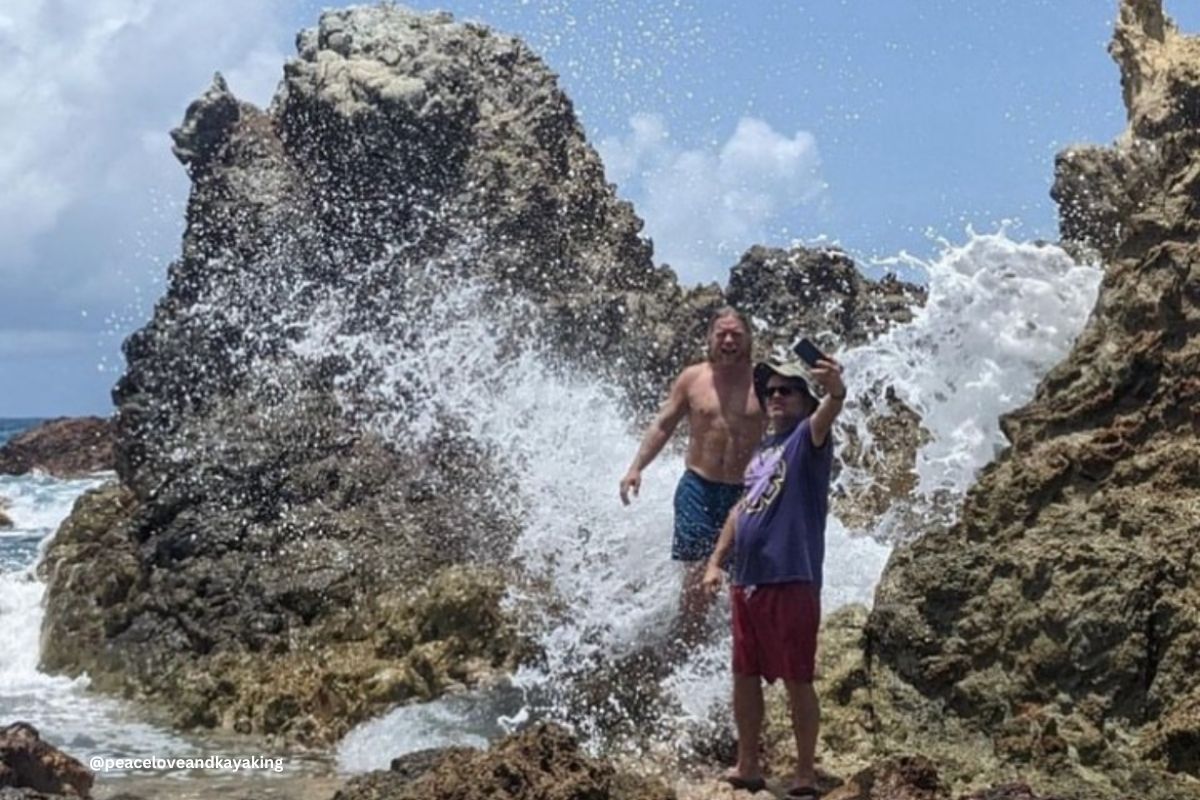 Two men are standing on rocks near the ocean taking a selfie.