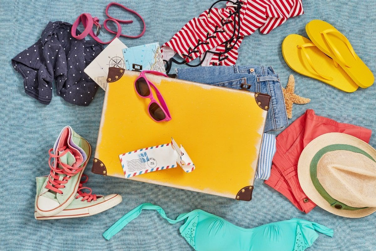 A yellow suitcase filled with clothes and flip flops on a blue carpet.