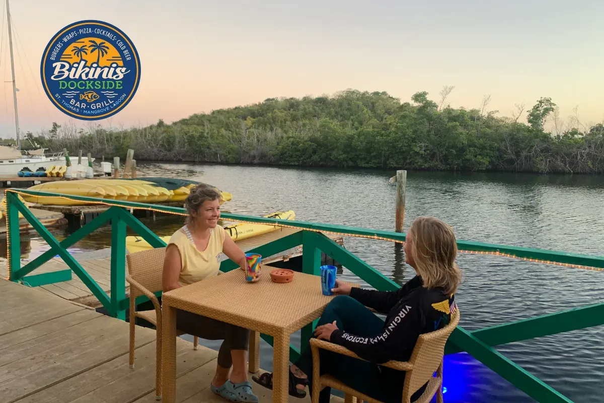 Two women are sitting at a table in front of a body of water.