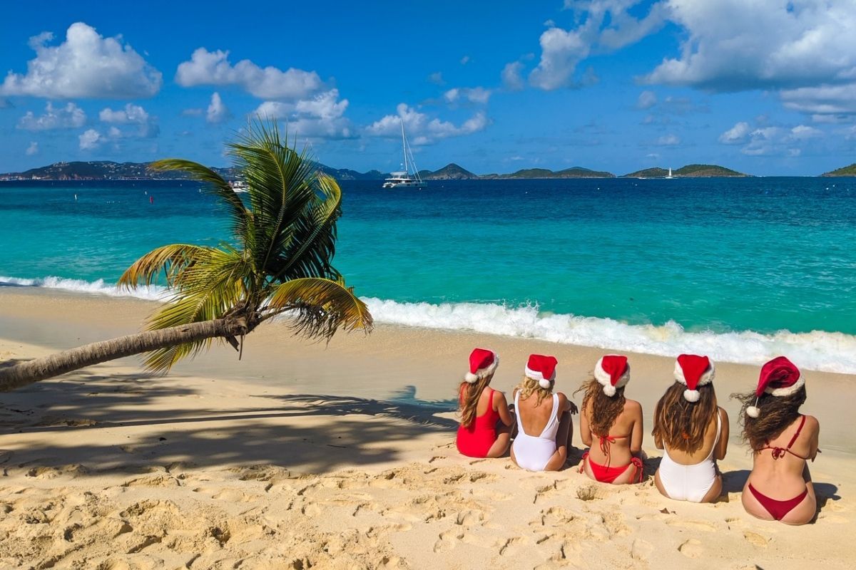 A group of women wearing santa hats are sitting on a beach.