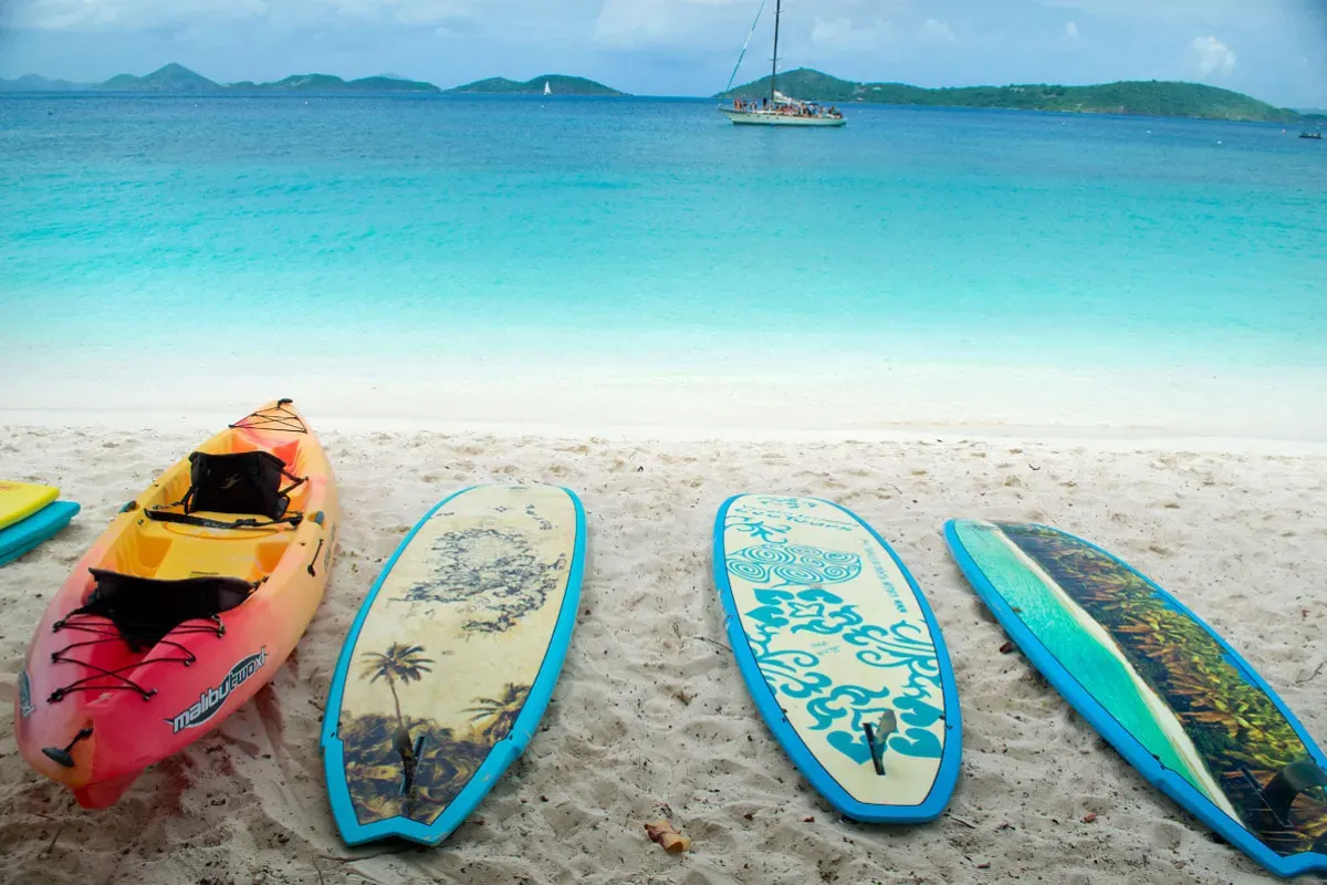 Surfboards and kayaks on a beach with a boat in the background