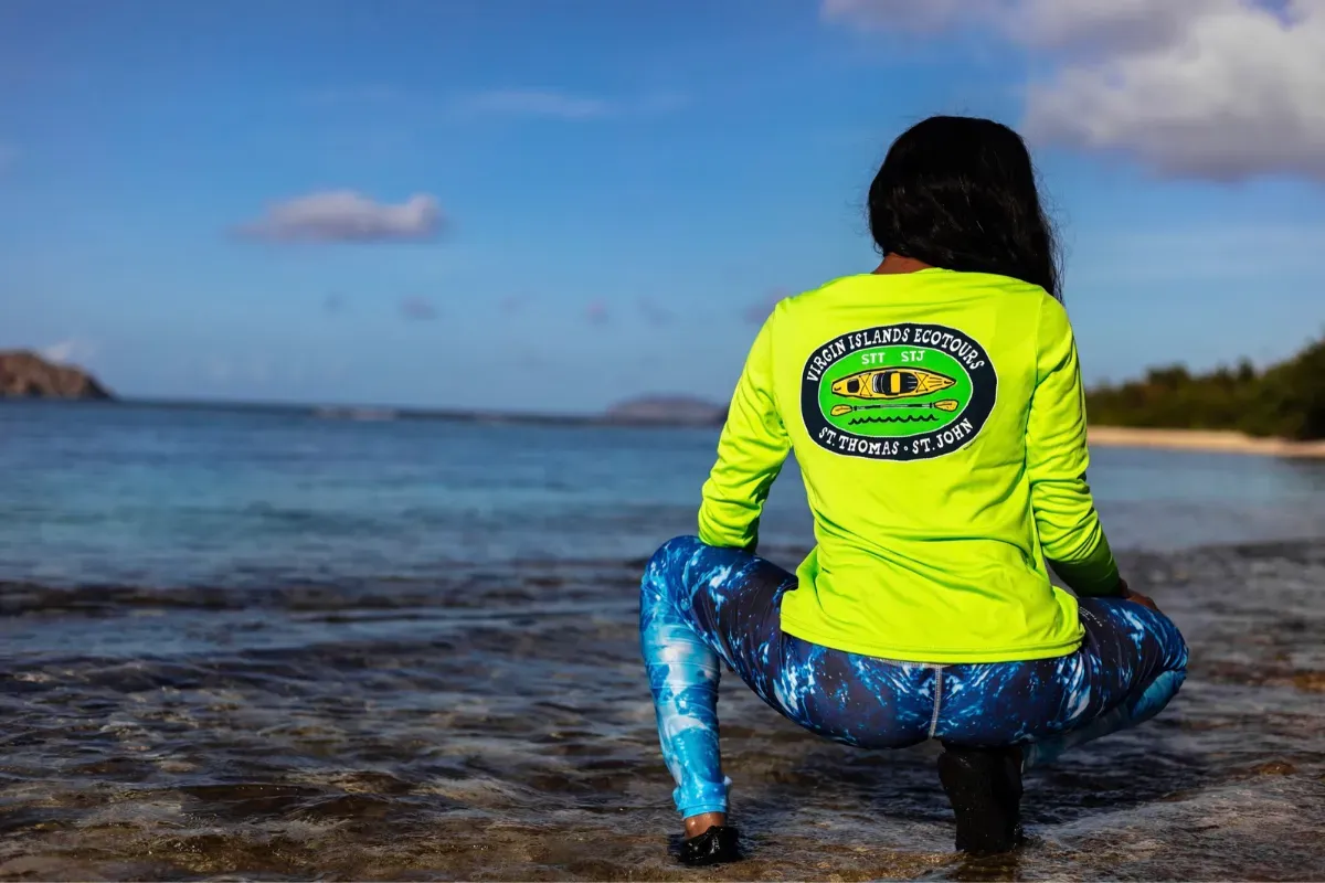 A woman is kneeling on the beach looking at the ocean.