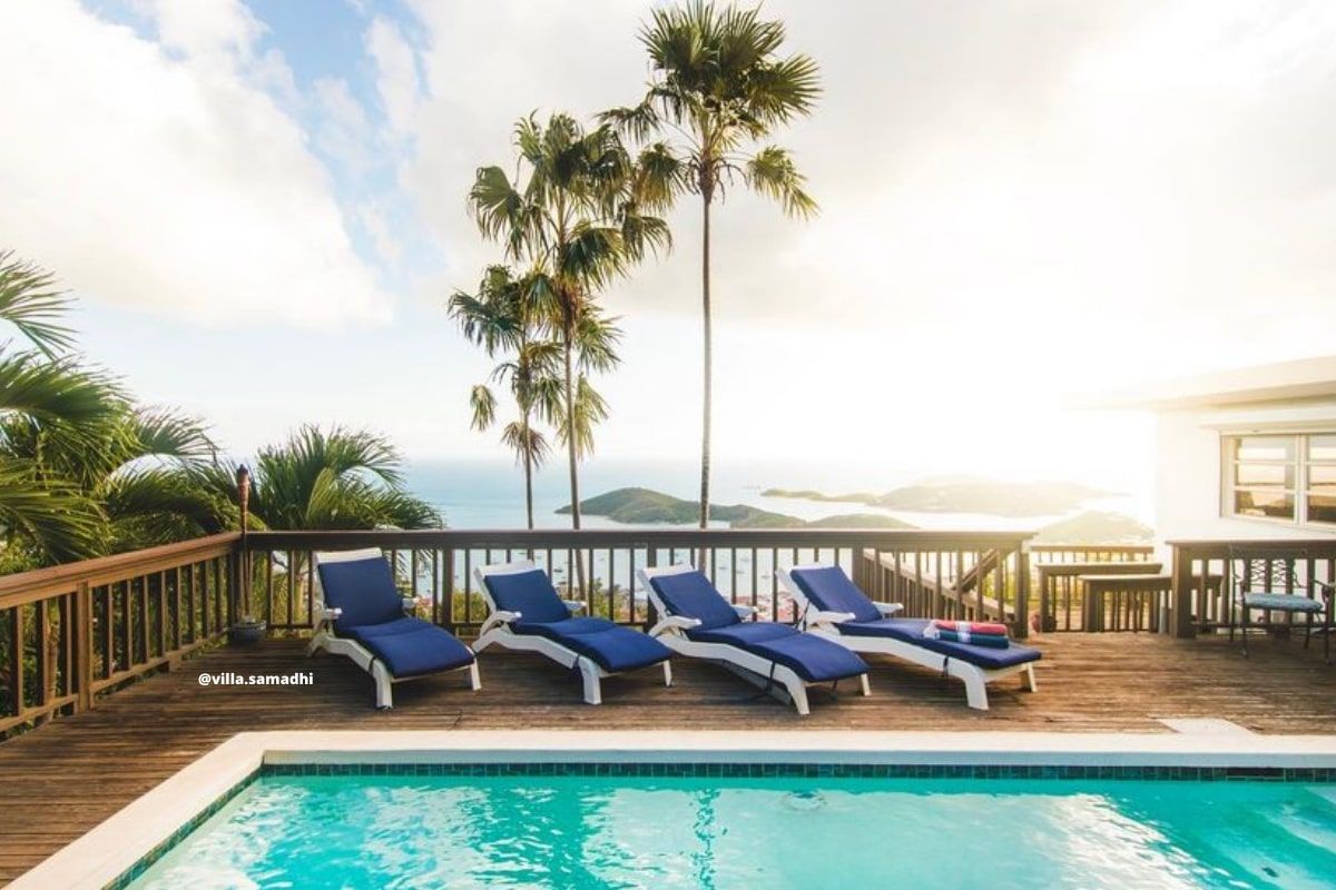 A swimming pool with blue lounge chairs on a deck overlooking the ocean.