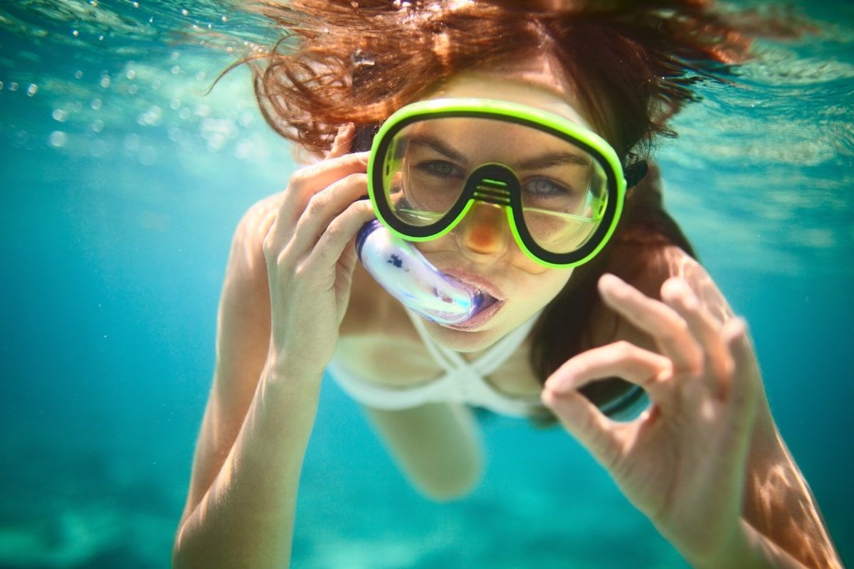 A woman is swimming underwater wearing a mask and giving the ok sign.