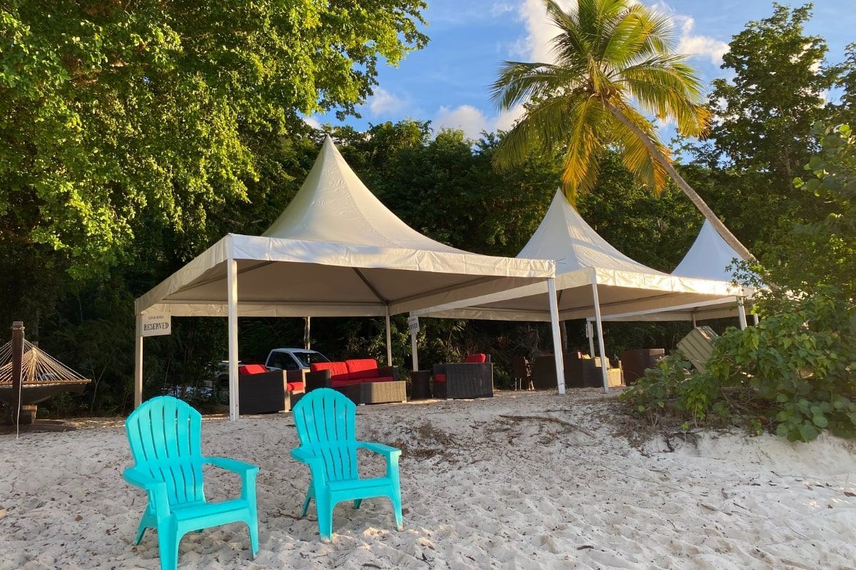 Two blue chairs are sitting on a sandy beach in front of tents.