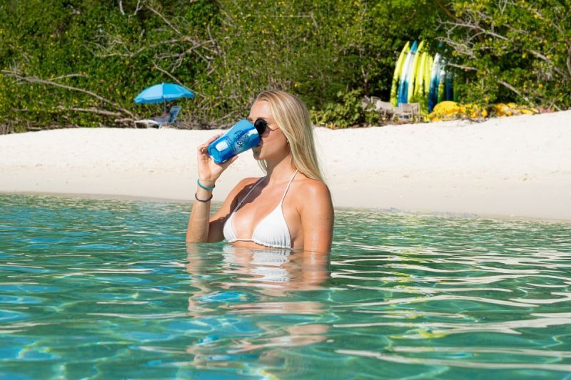 A woman in a bikini is drinking from a blue cup in the ocean.