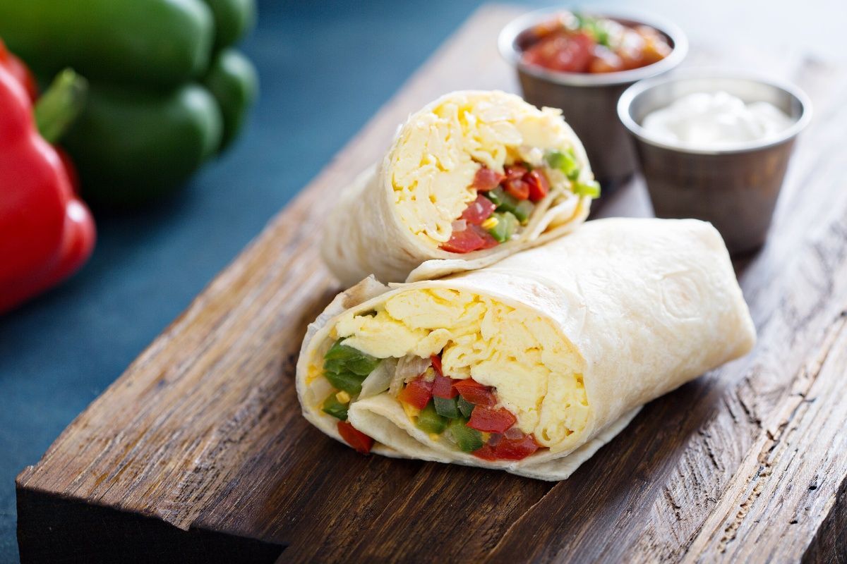 Two burritos are cut in half on a wooden cutting board.