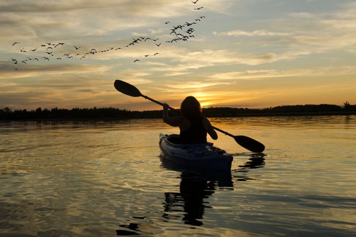 A person is paddling a kayak on a lake at sunset