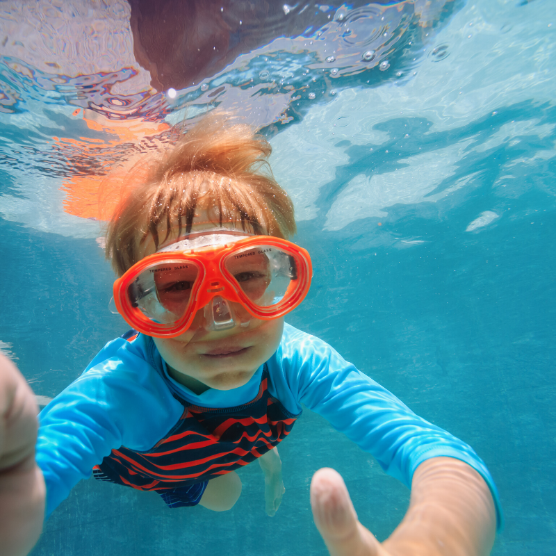 A young boy wearing goggles is swimming underwater