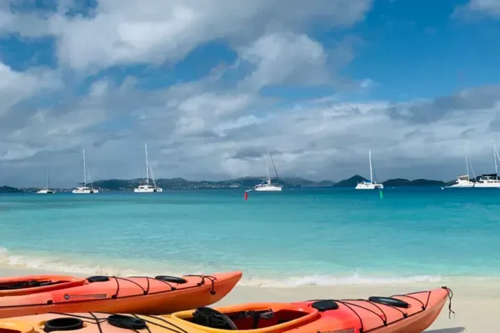 Two kayaks are sitting on a sandy beach next to the ocean.