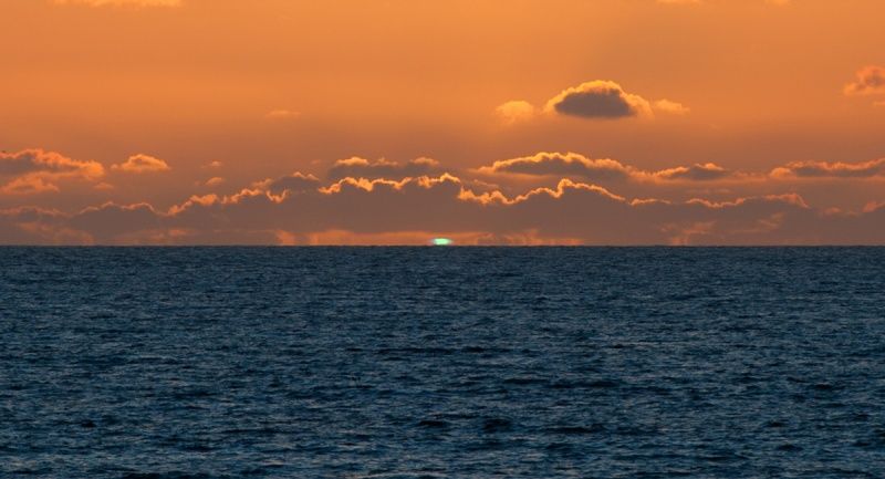 The sun is setting over the ocean with a green light in the sky.