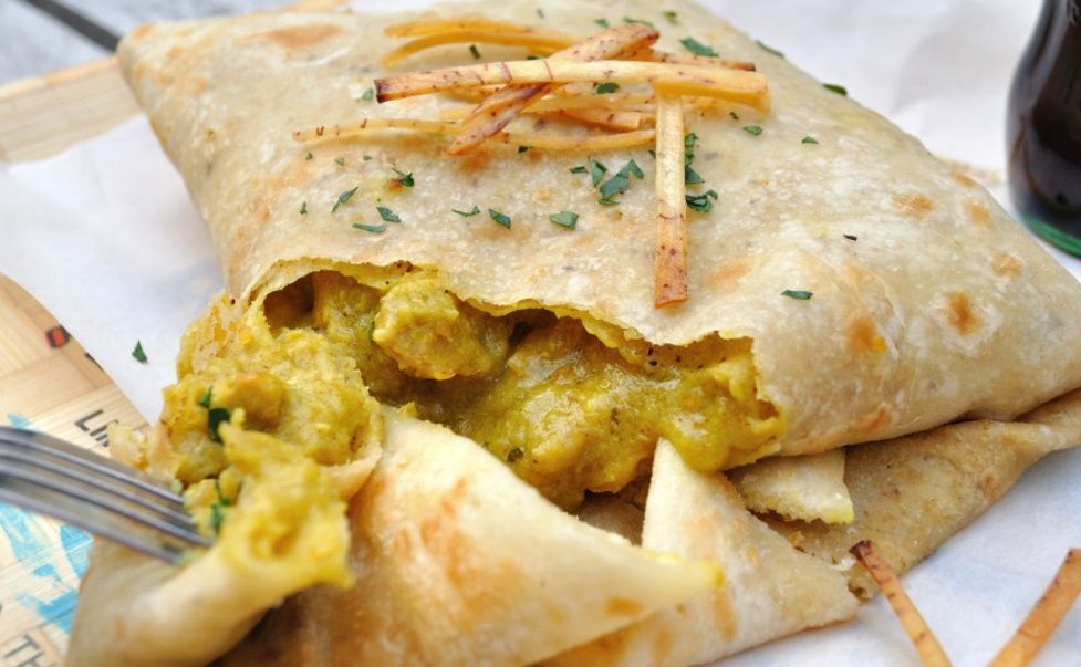 A close up of a wrap with french fries and a fork on a table.