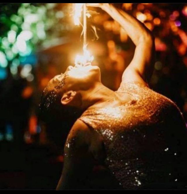 A woman in a sequined dress is holding a fire in her mouth.