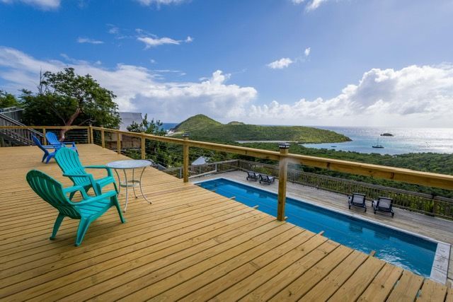 A wooden deck with chairs and a table overlooking a swimming pool.