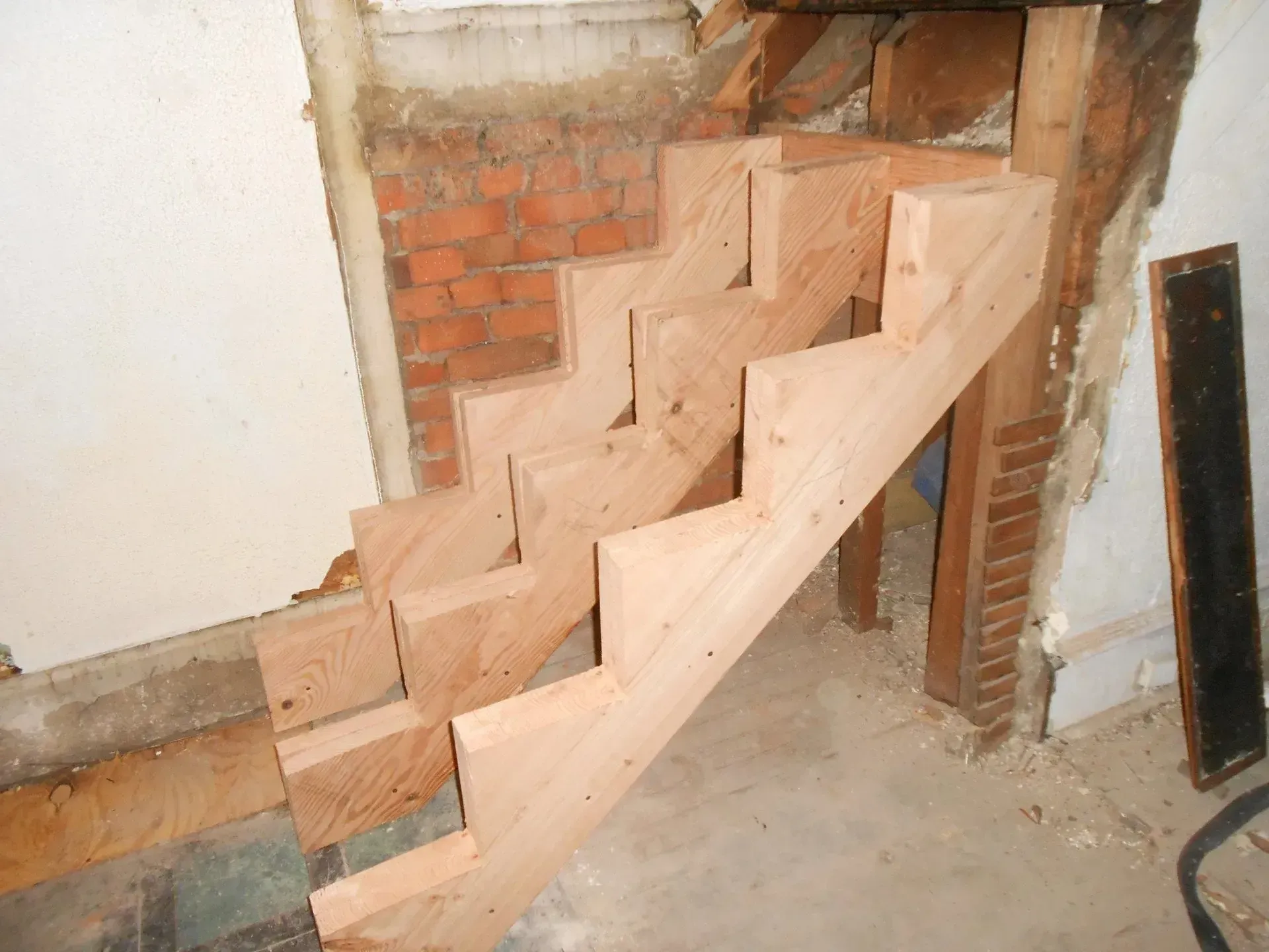 A wooden staircase is being built in a room next to a brick wall.