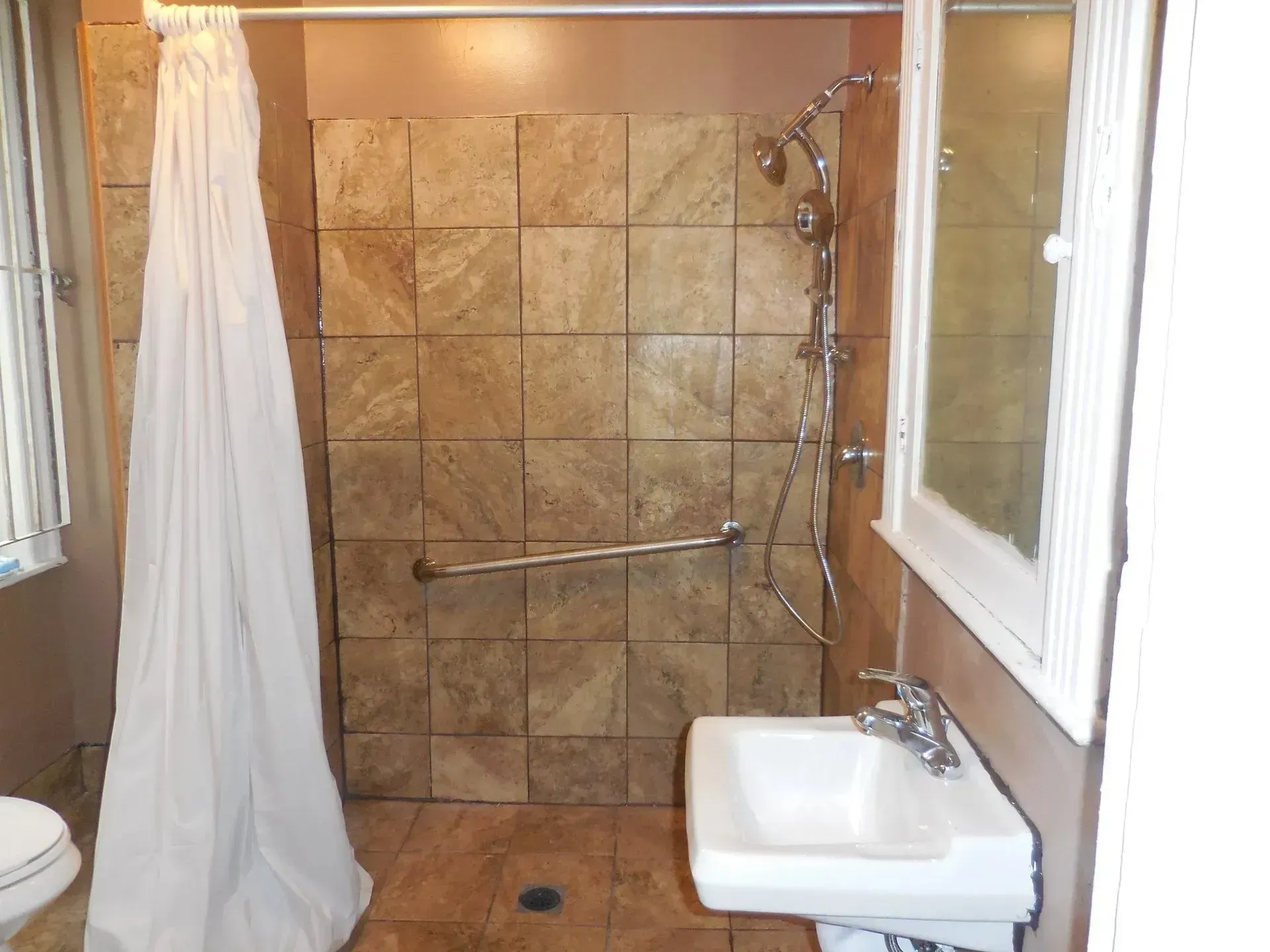 A bathroom with a sink , toilet , shower and mirror.