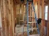 A person is standing on a ladder in a room under construction.