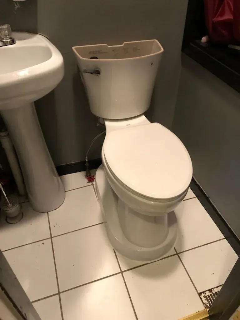 A toilet is sitting on a tiled floor next to a sink.