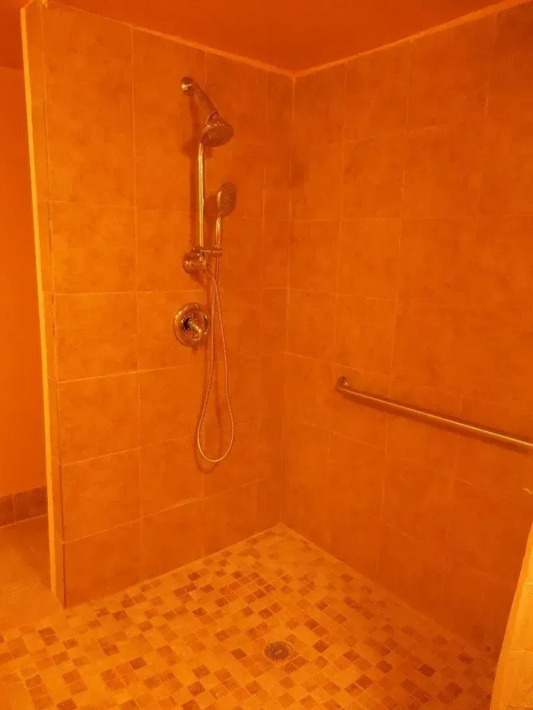 A walk in shower with a hand rail and a shower head.