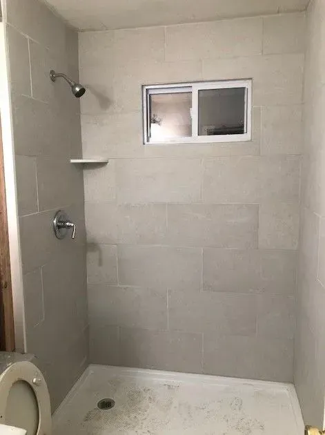 A bathroom with a shower , toilet and window.