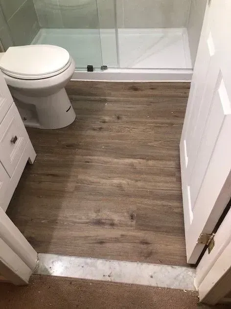 A bathroom with a toilet , sink , shower and wooden floor.