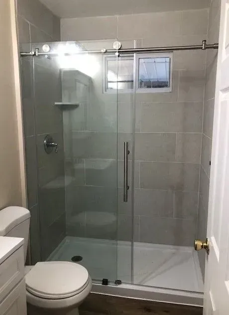 A bathroom with a toilet , shower and sliding glass door.