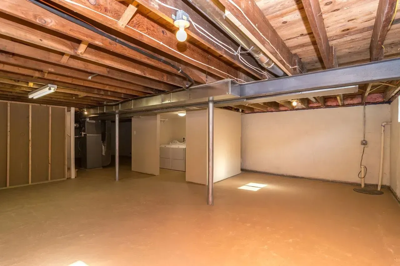 An empty basement with wooden beams and a laundry room.