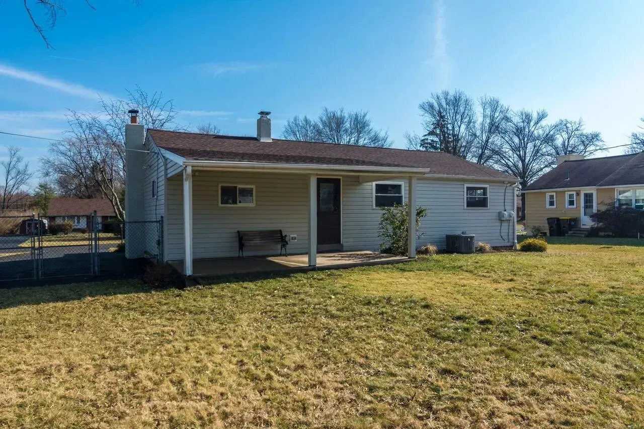 A small white house with a porch and a bench in the backyard.