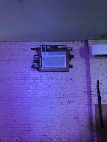 A brick wall with a window air conditioner hanging from it.