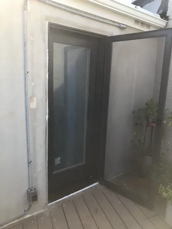A black screen door is open on a wooden deck.