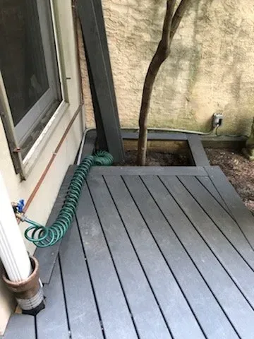A hose is sitting on a wooden deck next to a window.