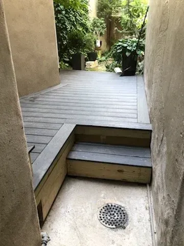 A wooden deck with stairs leading up to it next to a wall.