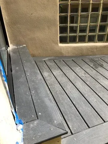 A close up of a wooden deck with a window in the background.