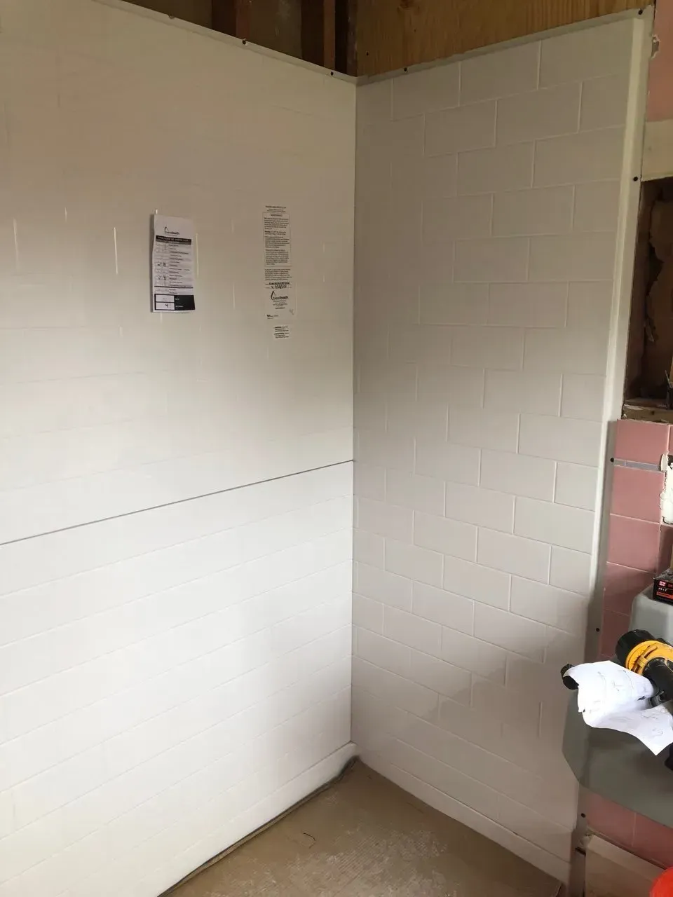 A corner of a room with a white wall and pink tiles.