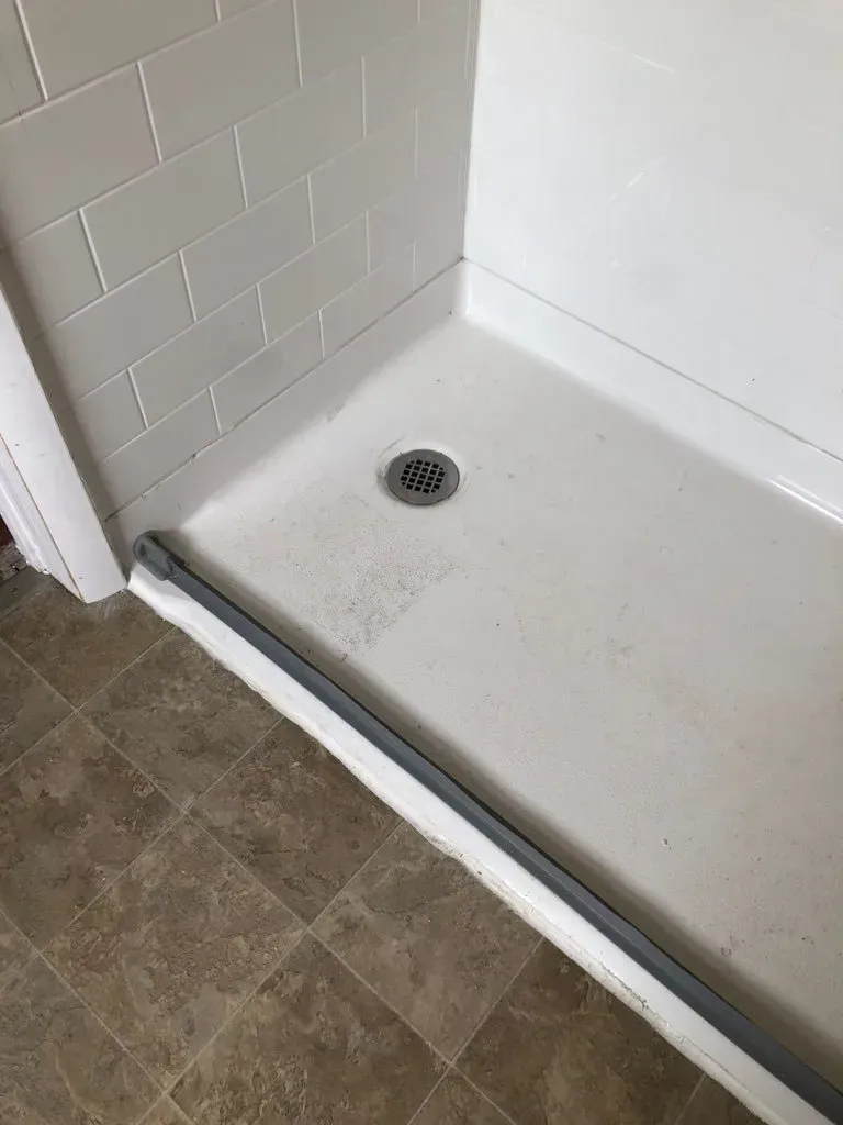 A white shower stall with a drain in a bathroom.