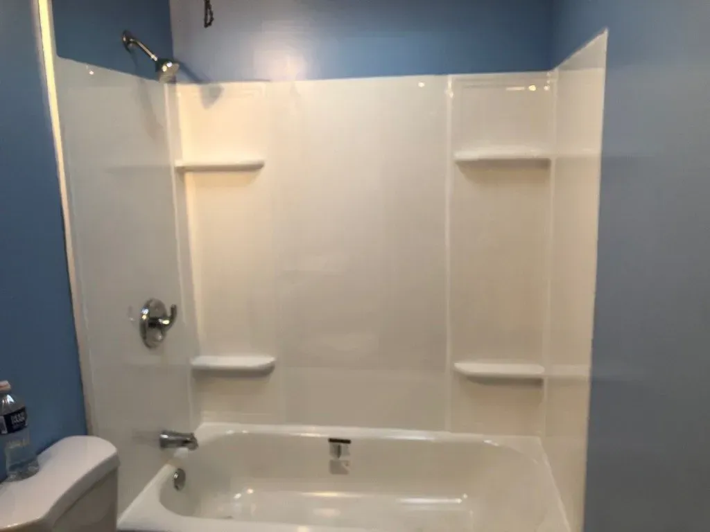 A bathroom with a bathtub , toilet , shower and shelves.