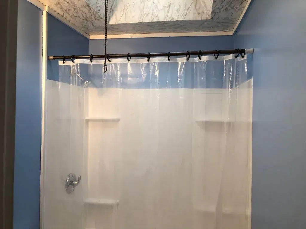 A bathroom with a clear shower curtain and blue walls