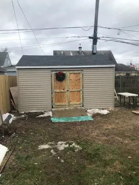 A shed with a wreath on the door is in the backyard of a house.