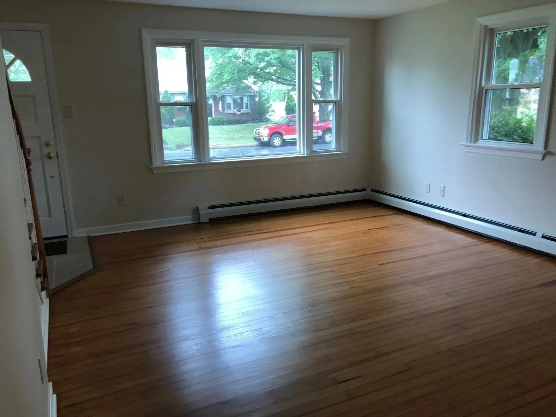 An empty living room with hardwood floors and two windows.