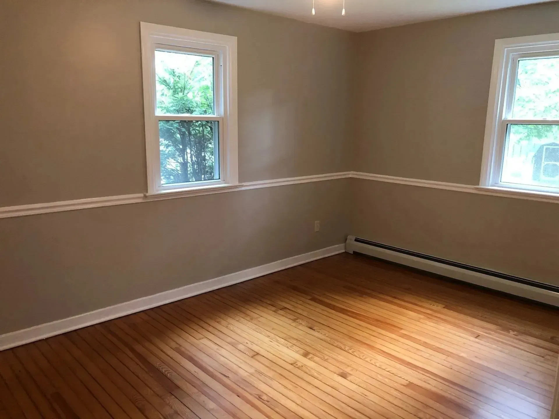 An empty room with hardwood floors and two windows.