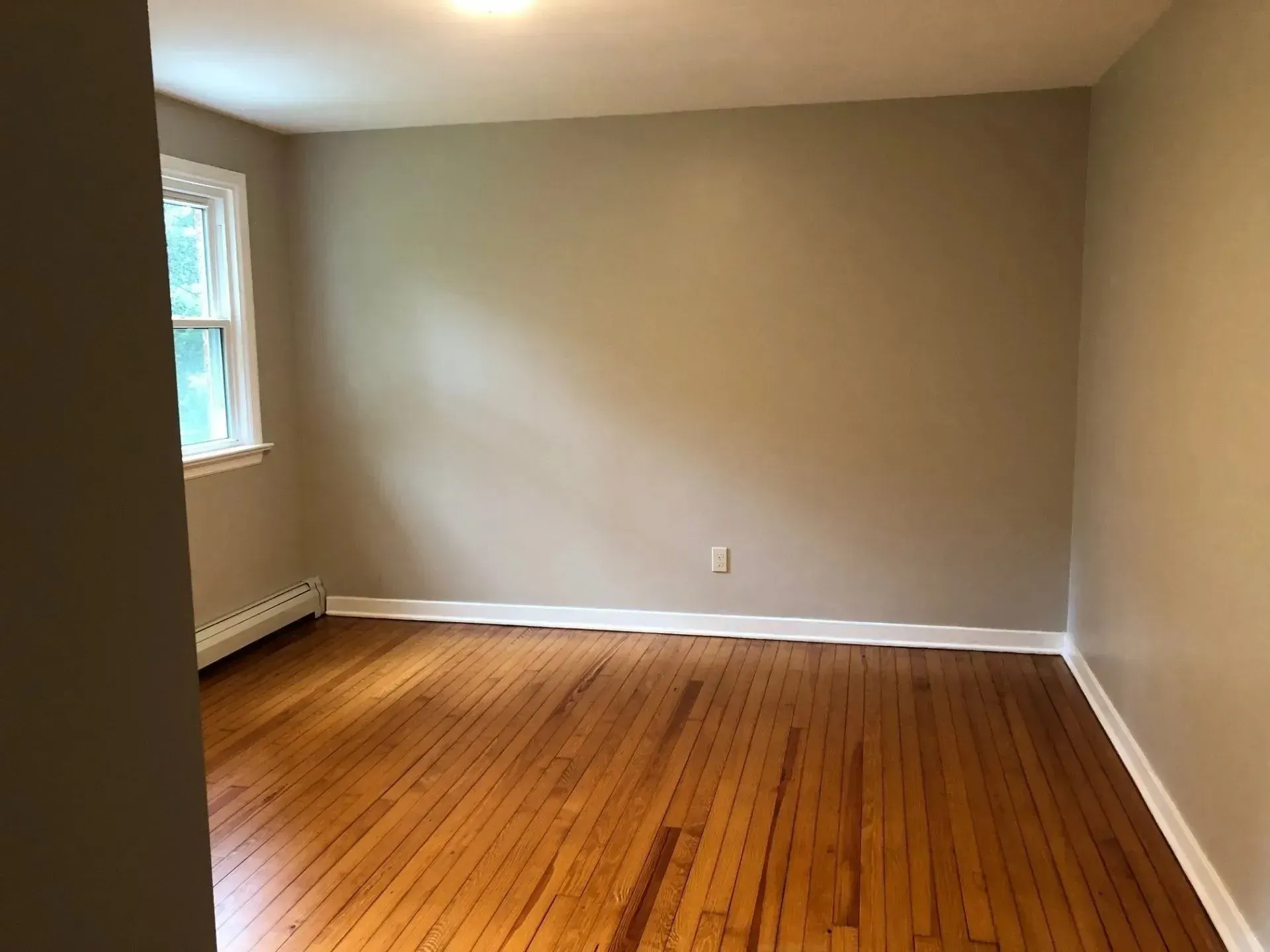 An empty room with hardwood floors and a window.