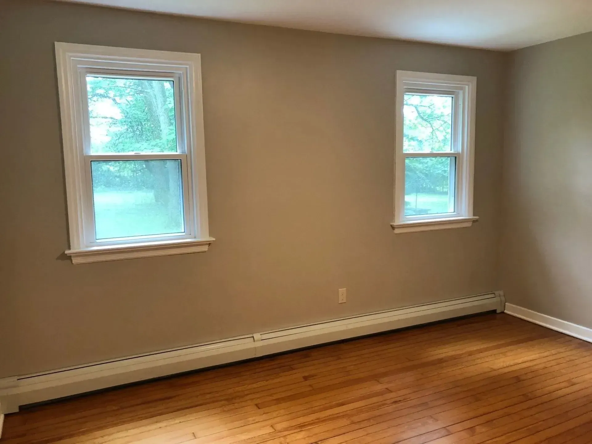 An empty room with two windows and hardwood floors.