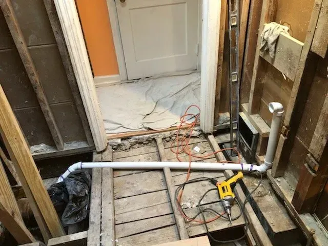 A drill is sitting on the floor of a room under construction.