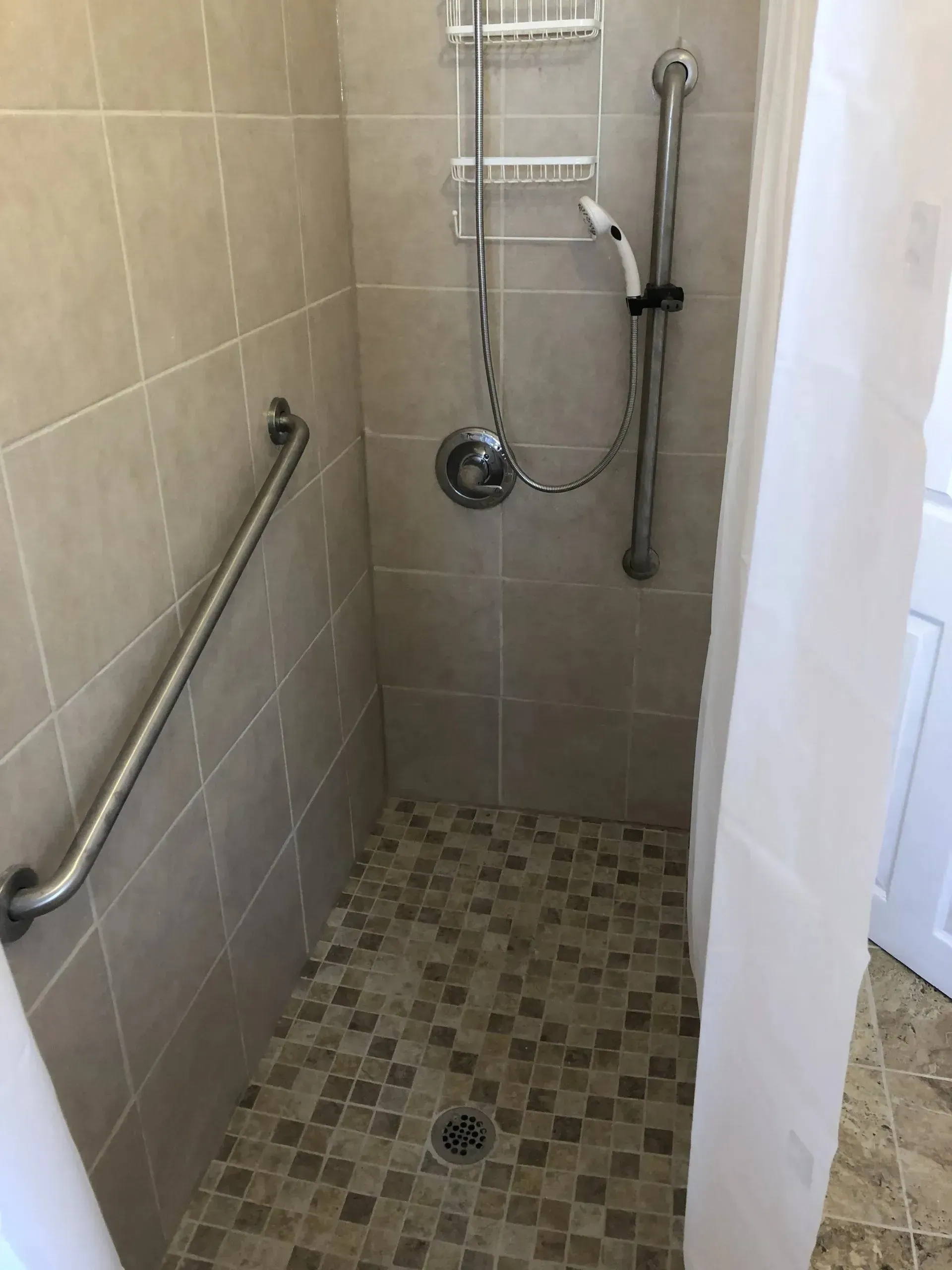 A walk in shower with a stainless steel railing and a shower head.