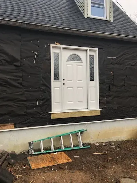 A white door is being installed on the side of a house.