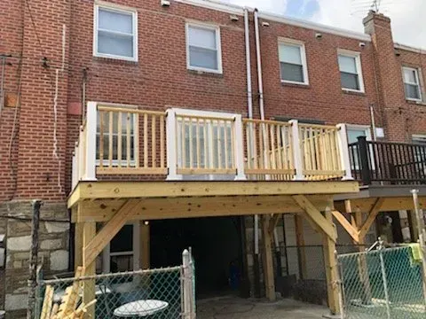 A wooden deck is being built on the back of a brick house.