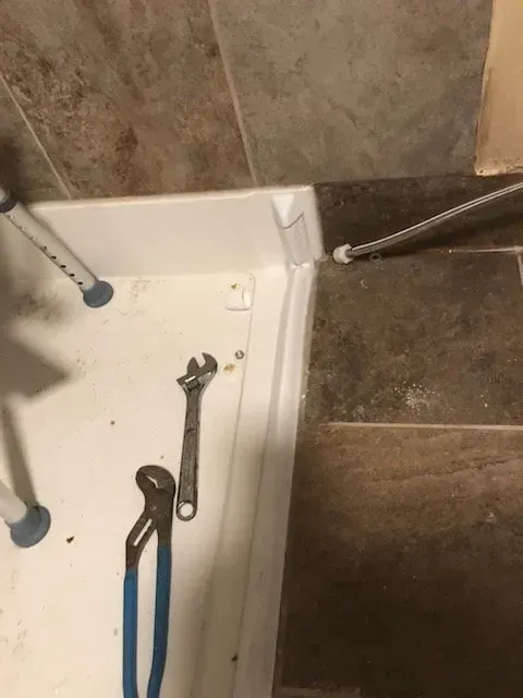 A shower stall with a wrench and pliers on it.