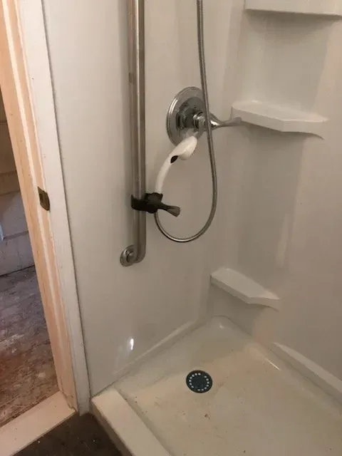 A shower stall with a hand rail and a shower head.