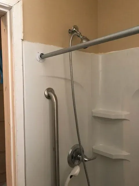 There is a shower with a hand rail and a shower head.