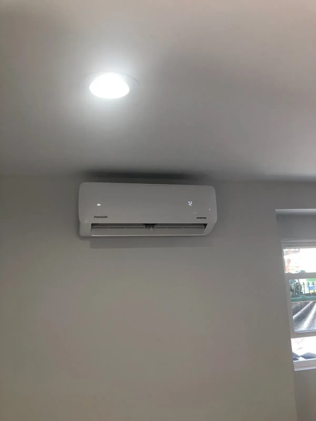 A white air conditioner is hanging from the ceiling in a room next to a window.